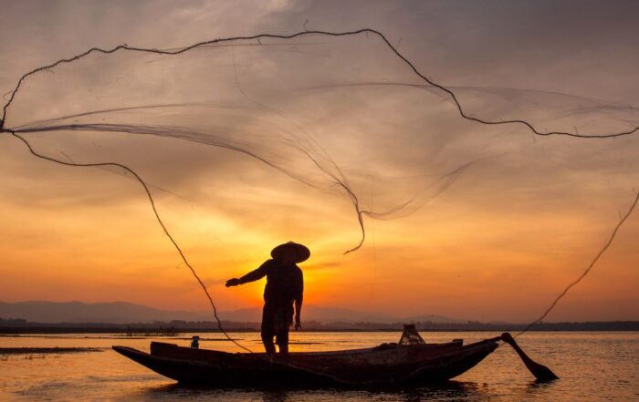 A stunning silhouette of a Vietnamese fisherman casting a traditional net on the river at sunset, representing the authentic culture of the Hoi An and Da Nang region.