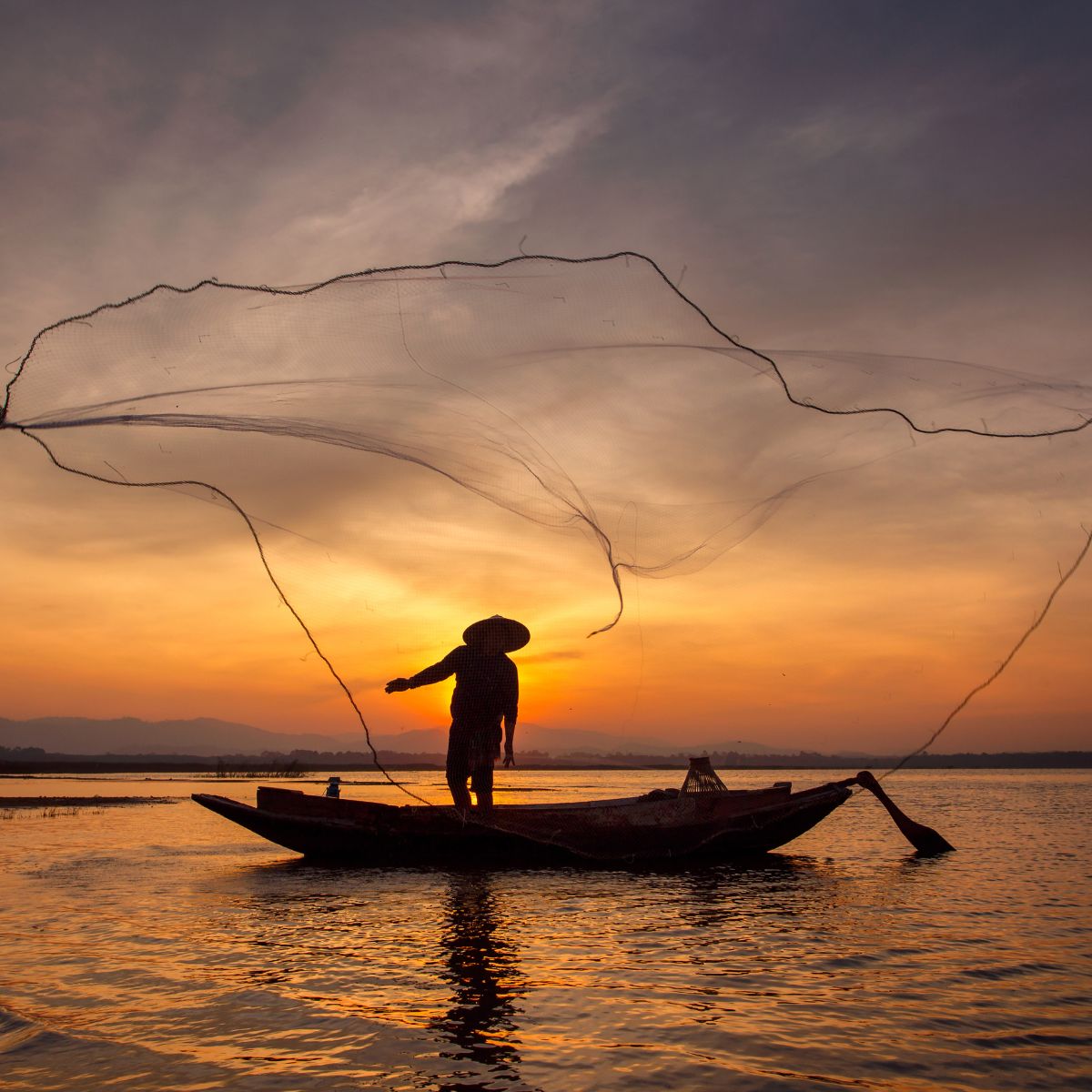 A stunning silhouette of a Vietnamese fisherman casting a traditional net on the river at sunset, representing the authentic culture of the Hoi An and Da Nang region.